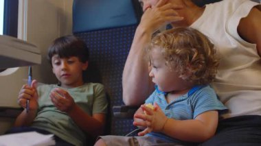 Anne, iki küçük çocukla birlikte trende gezerken, kucağında aile yolculuğu sırasında kucağında otururken bir ısırık almadan önce ablasına ikram ediyor.