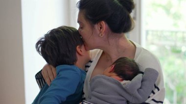 Büyük oğlan hem anne hem de yeni doğmuş bebeği öpüyor, sevgi ve bağla dolu şefkatli ve yürek ısıtan bir aile anı yaratıyor, anne ve kardeş arasındaki bağı vurguluyor.