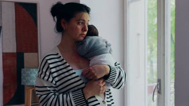 Anne pencerenin kenarında durmuş, yeni doğmuş bir bebek omuzunda, dışarıya bakıyor. Sahne, anne ve bebek arasındaki sakinlik, bağ ve huzur dolu anları aktarır..