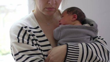 Anne, uyuyan bebeği göğsüne bastırıyor, rahat bir battaniyeye sarılıyor, sakin ve huzurlu bir ortamda hassas ve samimi bir yakınlaşma anı sergiliyor.