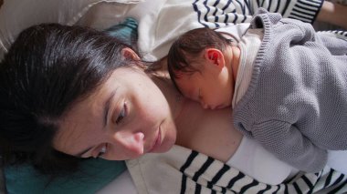 Anne, yeni doğmuş bebeği göğsünde uyurken, sevgi, sıcaklık ve anne ile çocuk arasındaki derin bağı yansıtan bir annelik anını düşünceli bir şekilde seyrediyor.