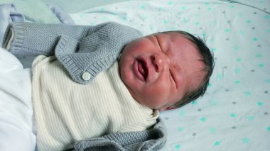 Yenidoğan bebek yerde yatarken ağlıyor, rahatsızlığını ifade ediyor ve hassas bir ifadeyle ilk zamanların duygusal anını yakalıyor.