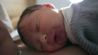Yeni doğan bebek annesinin göğsünde mutlu bir şekilde uyuyor. Yumuşak, doğal bir ışıkla yıkanmış. Huzurlu ve sıcak bir ortamda barışçıl ve samimi bir yakınlaşma anı yakalıyor.