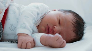 Yeni doğmuş bebek huzurlu bir şekilde uyuyor. Rahat bir yüz ifadesi ve nazik bir el hareketiyle. Bebeğin yüzüne yakın çekim ve küçük bir yumruk.