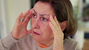 Şiddetli baş ağrısı çeken bir kadın, gergin bir ifadeyle parmaklarını şakaklarına bastırıyor. Kapalı gözler, çatık kaşlar, derin konsantrasyon ve belirgin zihinsel gerginlik, duygusal acı.