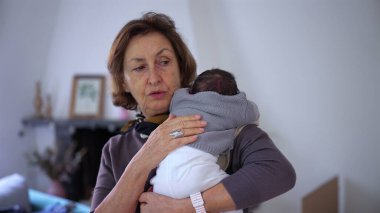 Büyükannem yeni doğmuş bir bebeği omzunda tutuyor, bebeği nazikçe okşuyor ve rahatlatıyor, şefkatli ve samimi bir sevgi ve ilgi anı yakalıyor..