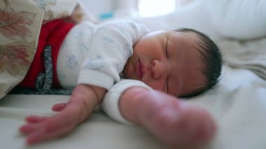 Yeni doğmuş bebek, kollarını uzatarak mışıl mışıl uyuyor. Rahatlamış ve huzurlu bir yüz ifadesi sergiliyor..