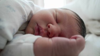 Yeni doğan bebek el ve ayakla uyuyor. Bebeklik döneminin hassas ve nazik doğasını vurguluyor..