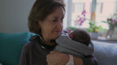 Anneanne yeni doğmuş bir bebeği omzunda tutuyor, huzurlu bir ifadeyle, bir sevgi ve bağ anını yakalıyor..