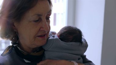 Anneanne yeni doğmuş bir bebeği omzuna yakın tutuyor, huzurlu bir ifadeyle, sevgi ve bağın hassas bir anını yakalıyor..