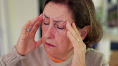 Şiddetli baş ağrısı çeken bir kadın, gergin bir ifadeyle parmaklarını şakaklarına bastırıyor. Kapalı gözler ve çatık kaşlar, derin konsantrasyon ve belirgin zihinsel gerginlik, duygusal acı - SD 480p