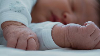 Bebek arka planda huzur içinde uyurken, yeni doğmuş bir bebeğin minik yumruklarına yakın çekim..