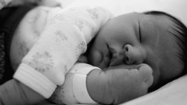 Yeni doğmuş bebeğe yakın plan. Yatakta huzur içinde uyuyor. Eli yüzünün yanında dinleniyor. Tek renkli bebeğin sakin ifadesi ve yumuşak, narin özellikleri..