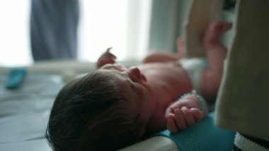 Anne yeni doğmuş bebeğine şefkatle bakıyor, bebeğe giysi giydiriyor, anne şefkati ve sevgi dolu bir anı ev ortamında yakalıyor..