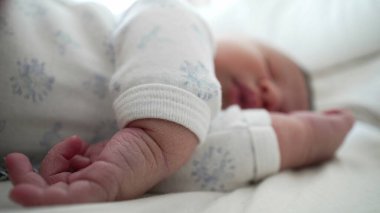 Yeni doğmuş bir bebeğin yakın planda uyuması eline odaklanır, çocukluk döneminin hassas ve hassas detaylarını huzurlu bir ortamda yakalar..