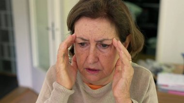 Olgun bir kadın yoğun bir baş ağrısı ya da stres yaşıyor, iki eliyle başını tutuyor, rahatsızlık ve endişelerini dile getiriyor. Yüz kırışıklıkları ve konsantrasyon, fiziksel ya da duygusal acı - SD 480p