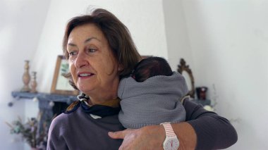 Büyükannem yeni doğmuş bir bebeği omzunda tutuyor, bebeği nazikçe okşuyor ve rahatlatıyor, şefkatli ve samimi bir sevgi ve ilgi anı yakalıyor..