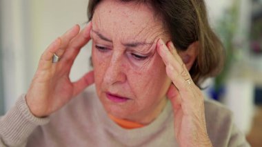 Şiddetli baş ağrısı çeken bir kadın, gergin bir ifadeyle parmaklarını şakaklarına bastırıyor. Kapalı gözler, çatık kaşlar, derin konsantrasyon ve belirgin zihinsel gerginlik, duygusal acı.