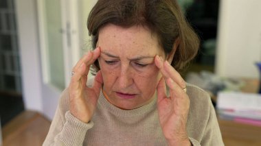 Olgun bir kadın yoğun bir baş ağrısı ya da stres yaşıyor, iki eliyle başını tutuyor, rahatsızlık ve endişelerini dile getiriyor. Yüz kırışıklıkları ve konsantrasyon, fiziksel ya da duygusal acı - SD 480p