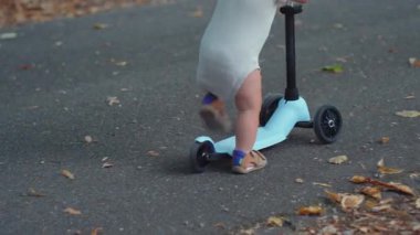 Küçük çocuk asfalt yolda mavi scooter sürüyor, ileri doğru iterken dengede duruyor, hareketli ve enerjik açık hava anı