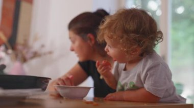 Bebek kendini elleriyle beslerken anne başka tarafa bakıyor. Sıradan bir aile yemeği sırasında bağımsız yemek, evde otantik bir yaşam tarzı..
