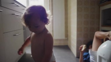 Yürüyen Çocuk Mutfak zemininde oturuyor Metal Kahve Demliği açıyor ve Odaklanmış ve Meraklı İfadeyle Nesneyi Keşfederken Oynuyor