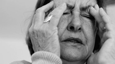 Yaşlı kadın yakın plan, gözleri kapalı, iki eli şakaklarına baskı yapıyor, derin kırışıklıklar ve acı dolu ifade, şiddetli stres veya baş ağrısı SD 480p