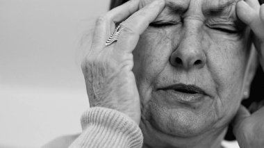 Yaşlı kadın yakın plan, gözleri kapalı, iki eli şakaklarına bastırıyor, derin kırışıklıklar ve acı dolu ifade, şiddetli stres ya da baş ağrısı