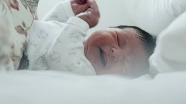 Yeni doğmuş bebek yatakta ağlıyor, rahatsız edici bir şekilde elini kaldırıyor. Bebeğin yüzünde sıkıntı var ve jestler ajitasyon-SD 480p gösteriyor.