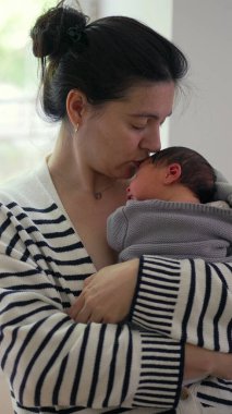 Anne yeni doğmuş bebeğini göğsüne yakın tutuyor, şefkatli bir ifadeyle aşağıya bakıyor. Anne ve çocuk arasındaki güçlü bağ sakin, kapalı alan ayarlı SD 480p