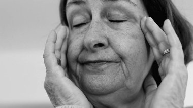 Yaşlı kadın yakın plan, gözleri kapalı, iki eli şakaklarına baskı yapıyor, derin kırışıklıklar ve acı dolu ifade, şiddetli stres veya baş ağrısı SD 480p