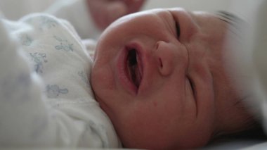 Yeni doğmuş bebek yatakta yatıyor, gözleri sonuna kadar açık, merakla etrafı keşfediyor. Bebek yüzü merak ve ilgi gösteriyor, doğal, yumuşak ışık içeride.