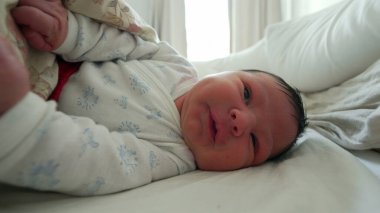 Yeni doğmuş bebek battaniyenin altında hareket ediyor, tuhaf bir ifadeyle yüzünü buruşturuyor, SD 'nin ilk ayındaki tipik hareketleri ve ifadeleri vurguluyor.