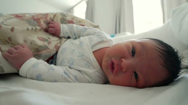 Çiçekli bir battaniyenin altında dinlenen yeni doğmuş bebek, çevresini keşfederken yüzünü buruşturuyor ve el kol hareketi yapıyor, hayatın ilk ayı ve erken gelişim taşları - SD 480p