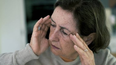 Başı kapalı, gözleri kapalı, şiddetli baş ağrısıyla boğuşan yaşlı bir kadın. Yüz ifadesi ve çatık kaş, yoğun zihinsel ve duygusal gerginlik SD 480p