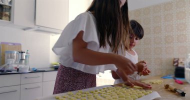 Kız ve erkek mutfakta para kazanıyor, anne arka planda, çocuklar aşçılık faaliyetinde, aile çalışması, parlak ev ortamı, etkileşimli yemek pişirme anı