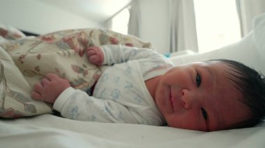 Çiçekli bir battaniyenin altında dinlenen yeni doğmuş bebek, çevresini keşfederken yüzünü buruşturuyor ve işaret ediyor, hayatın ilk ayı ve erken gelişim kilometre taşları.