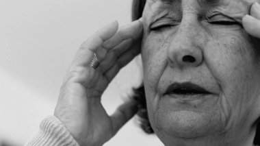 Yaşlı kadın yakın plan, gözleri kapalı, iki eli şakaklarına baskı yapıyor, derin kırışıklıklar ve acı dolu ifade, şiddetli stres veya baş ağrısı SD 480p