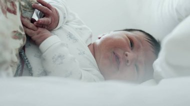 Yeni doğmuş bebek yatakta ağlıyor, rahatsız edici bir şekilde elini kaldırıyor. Bebeğin yüzünde sıkıntı var ve jestler ajitasyon-SD 480p gösteriyor.