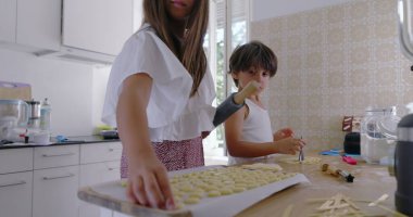 Çocuklar mutfakta hamur hazırlıyor, kız odaklanıyor, oğlan asistanı, aile yemekleri aktivitesi, anne arka planda, parlak ev dekorasyonu, etkileşimli öğrenme anı, takım çalışması