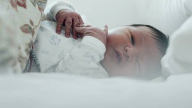 Yeni doğmuş bebek yatakta ağlıyor, rahatsız edici bir şekilde elini kaldırıyor. Bebeğin yüzünde sıkıntı var ve jestler ajitasyon-SD 480p gösteriyor.