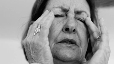 Yaşlı kadın yakın plan, gözleri kapalı, iki eli şakaklarına baskı yapıyor, derin kırışıklıklar ve acı dolu ifade, şiddetli stres veya baş ağrısı SD 480p