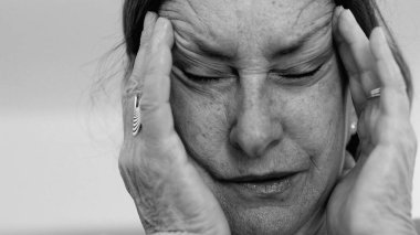 Yaşlı kadın yakın plan, gözleri kapalı, iki eli şakaklarına baskı yapıyor, derin kırışıklıklar ve acı dolu ifade, şiddetli stres veya baş ağrısı SD 480p