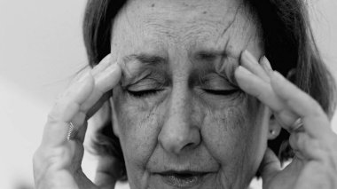 Yaşlı kadın yakın plan, gözleri kapalı, iki eli şakaklarına baskı yapıyor, derin kırışıklıklar ve acı dolu ifade, şiddetli stres veya baş ağrısı SD 480p