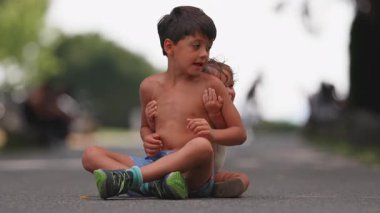 Ağabeyi yolda bağdaş kurmuş otururken, bebek ona arkadan sıkıca sarılıyor. Kardeşler arasında duygusal bir bağ, sevgi ve şevkat gösteriyor.