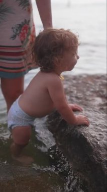 Sığ sularda, kayalık kıyılara yakın bir yerde duran küçük çocuk taşın kenarına tutunarak, tuhaf ifadeler takınarak, doğayı keşfederek, yazın açık havada aktiviteler yaparak, erken çocukluk gelişimiyle..