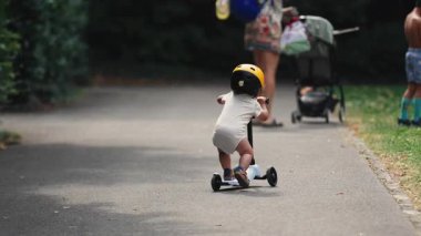 Bebek arabası ve ağabeyi ile annesine doğru scooter sürerken yaz parkı yolunda neşeli çocukluk titreşimleriyle neşeli bir aile havası hakimdi.