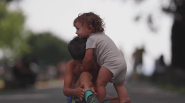 Bebek gibi kucaklaşan ağabeyi sırtüstü uzanıyor. Dışarıdaki aile ortamında kardeşlerin arasında duygusal bir bağ var.
