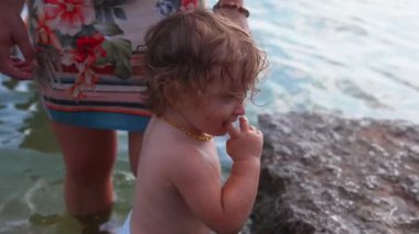 Yavru, kayalık kıyıya yakın sığ sularda dururken anne yakın durup denge için el ele tutuşurken ebeveyn korumasını, bakımını ve dışarıdaki güvenliğini gösteriyor.