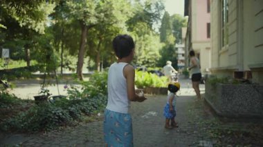 Su balonunu annesine doğrultan genç bir çocuk neşeli açık hava su savaşı sırasında küçük çocuk güneşli yaz gününde aile bağları kurma anını seyrediyor..